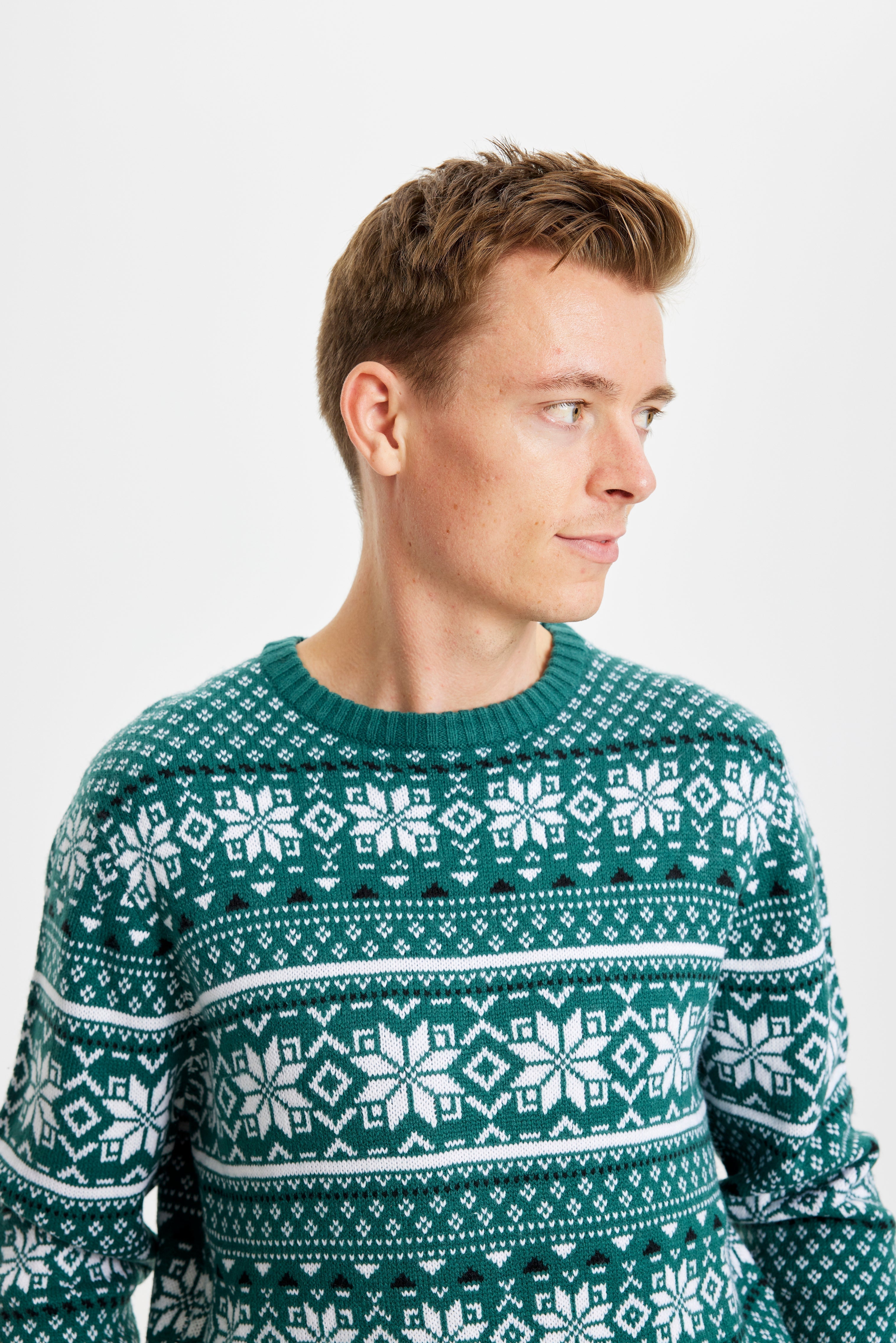 Homme posant, regardant de côté, portant un pull vert de Noël avec des flocons de neige.